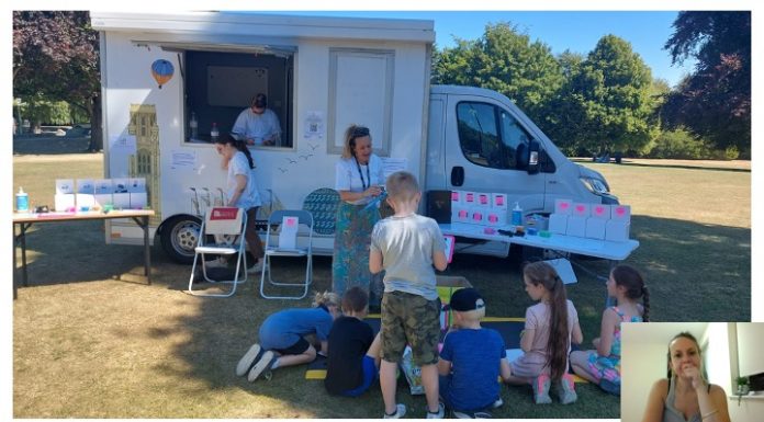 Van parked up on grassy area; adults and children sitting and standing around it participating in outreach event