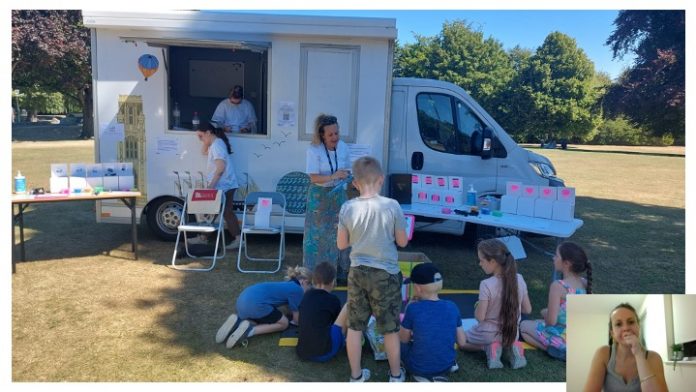 Van parked up on grassy area; adults and children sitting and standing around it participating in outreach event