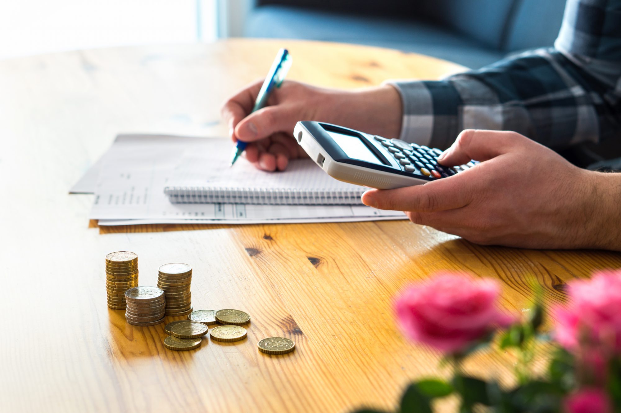 Person working at desk calculating cost of bills. Coins piled up next to them