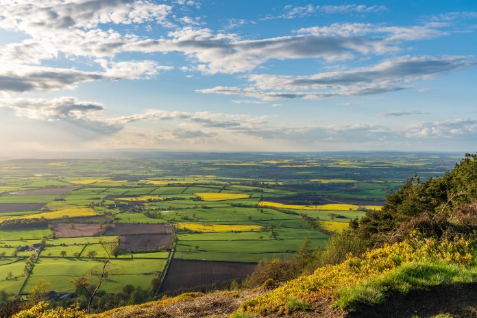 View from the Wrekin, near Telford, Shropshire, England, UK - looking northwest towards Leaton. Patchwork fields of green, yellow under cloudy blue sky
