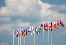 Flags on some of the major countries in the world rippling inn the wind against a cloudy blue sky