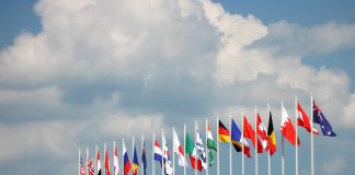 Flags on some of the major countries in the world rippling inn the wind against a cloudy blue sky