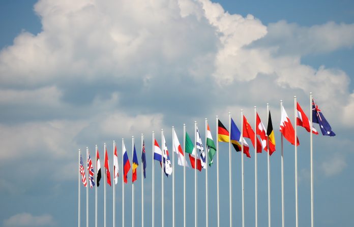 Flags on some of the major countries in the world rippling inn the wind against a cloudy blue sky