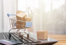 Mini shopping trolley sitting on top of laptop piled high full of mini cardboard boxes