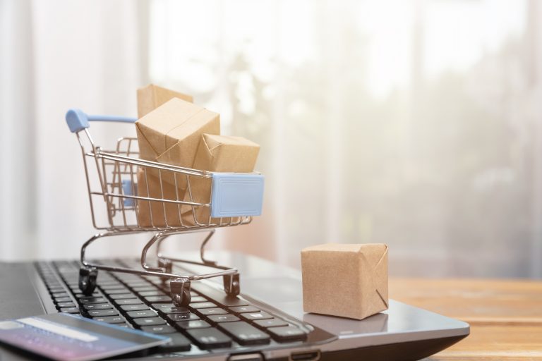 Mini shopping trolley sitting on top of laptop piled high full of mini cardboard boxes