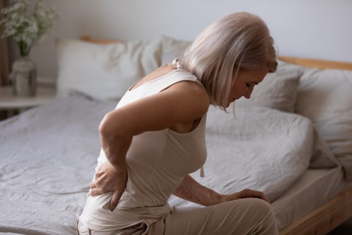 Older woman leaning over bed in pain
