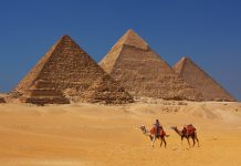 Egyptians pyramids and people on camels against a blue sky