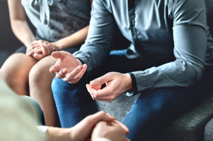 Close up photograph of man and woman sat next to each other at talking therapy session