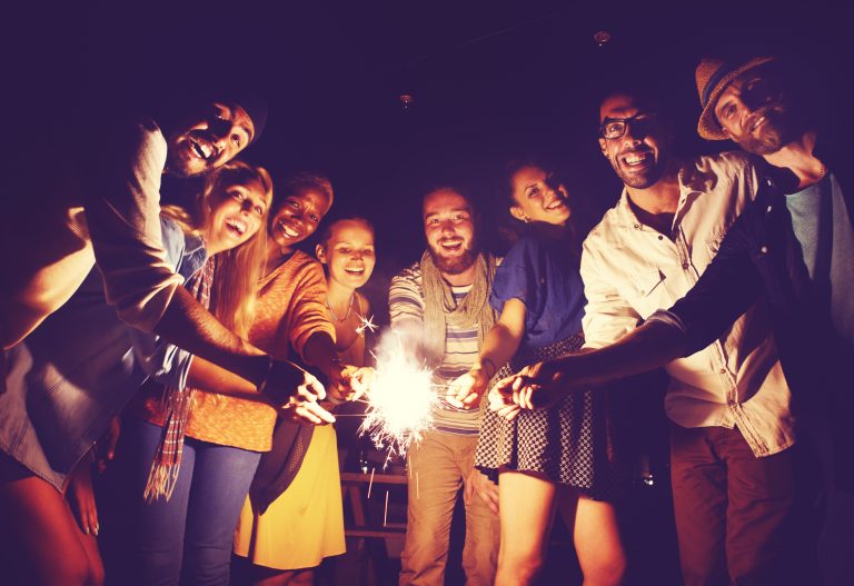 Group setting under dark sky using sparklers, happy faces, enjoying leisure time