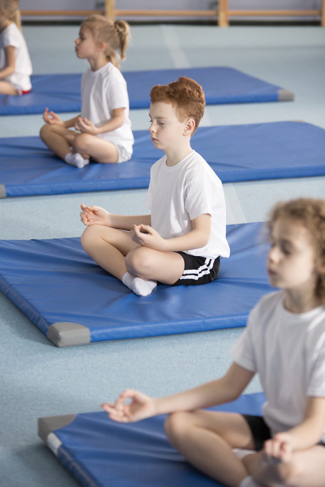 Elementary school pupil and other children sitting on mats with their legs crossed and eyes closed in relaxing meditation class