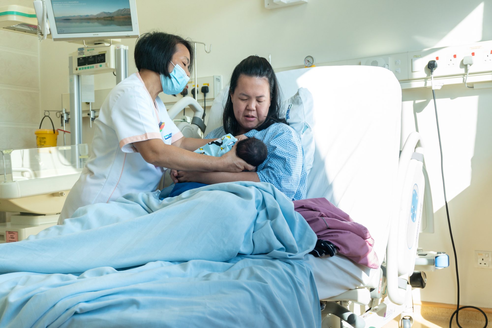 Midwife helping newborn baby and mother how to breastfeeding on Labour room hospital ward