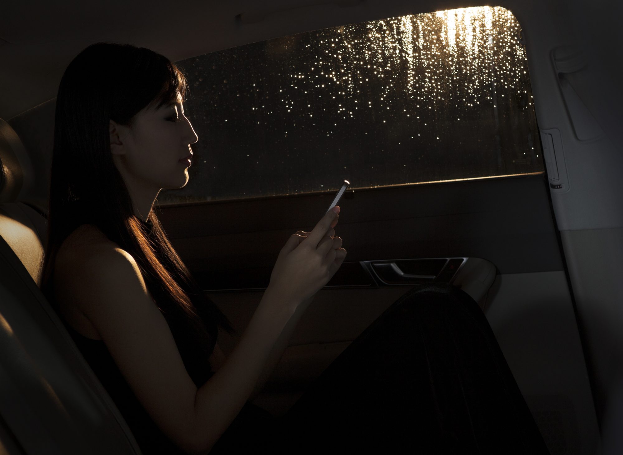 Young woman sitting in the car and texting on her phone on a rainy night in Beijing