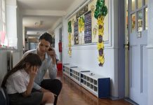 A female teacher sits consoling a young student in the corridor