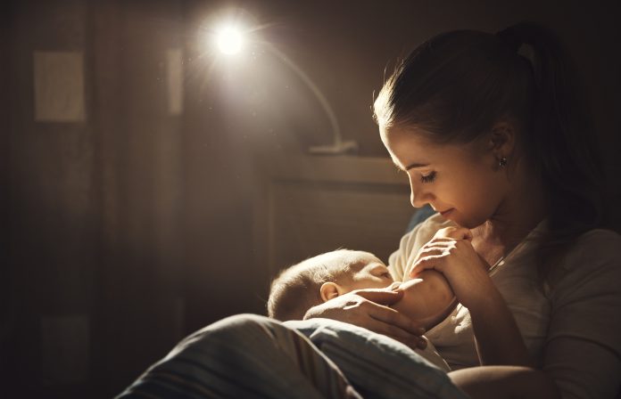Breastfeeding. mother feeding baby breast in bed dark night