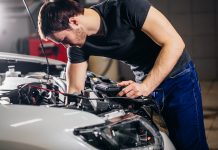 Electrician bending over bonnet of electric vehicle whilst doing electrical work, EV training