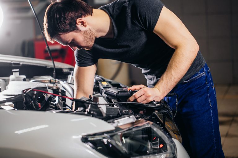 Electrician bending over bonnet of electric vehicle whilst doing electrical work, EV training