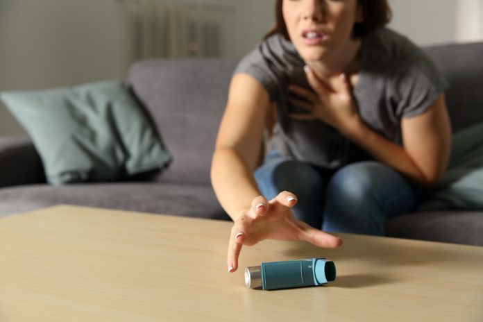 Woman suffering severe asthma attack reaching for inhaler on table