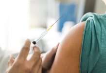 Vaccine or flu shot in injection needle next to person's arm, ready to be injected