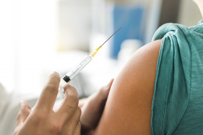 Vaccine or flu shot in injection needle next to person's arm, ready to be injected