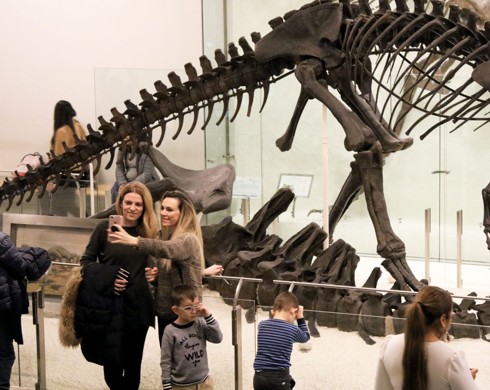 Women posing in front of dinosaur fossils at museum
