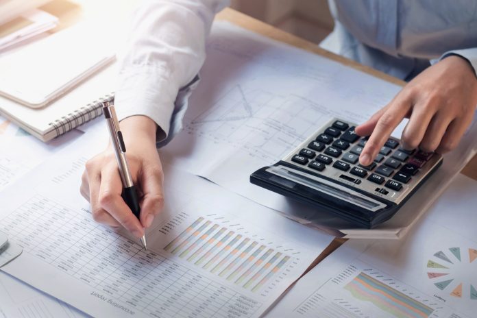 Person sitting at desk over spreadsheets working out sums on calculator