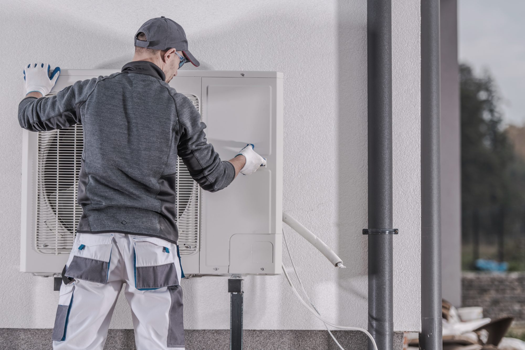 Man in work wear and cap fitting a heat pump on side of building