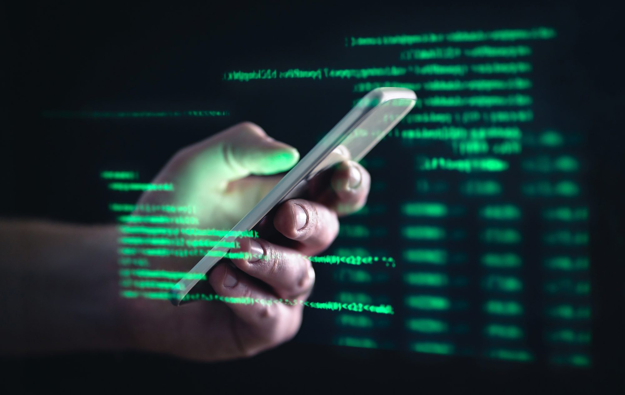 Person holding mobile phone against dark black background, green code writing over hand and phone