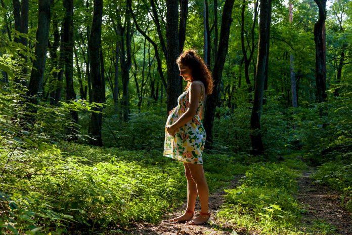 Pregnant woman posing with her bump in lush green forest