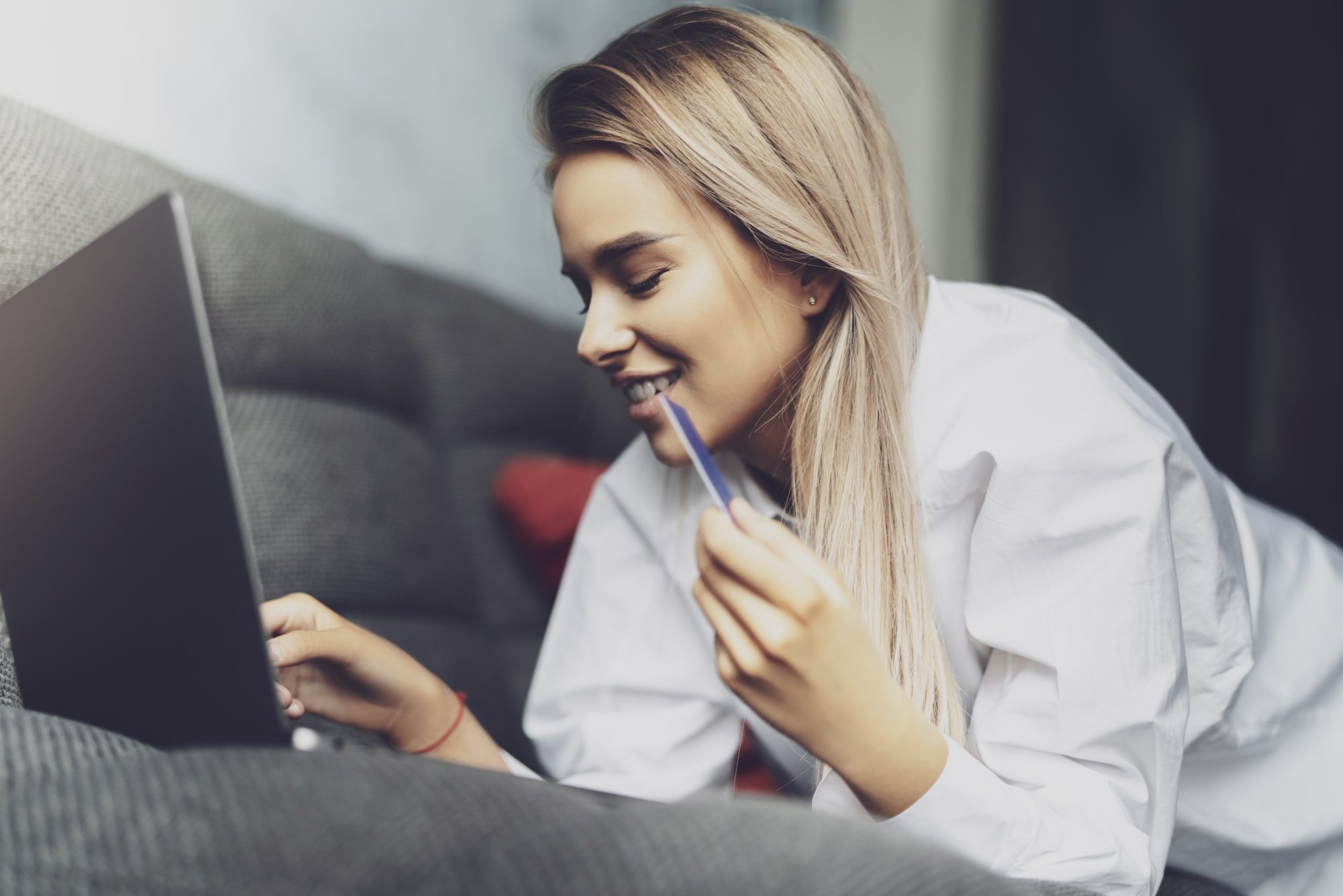 Young blonde woman leaning over laptop on sofa