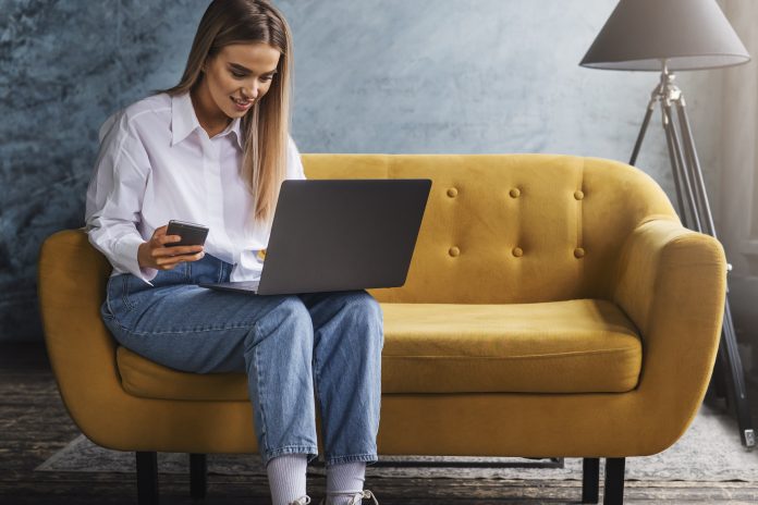 Woman learning new digital skills on laptop, sat on yellow couch