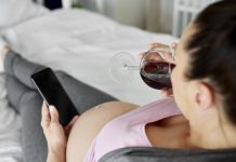 Heavily pregnant woman drinking glass of red wine in bed