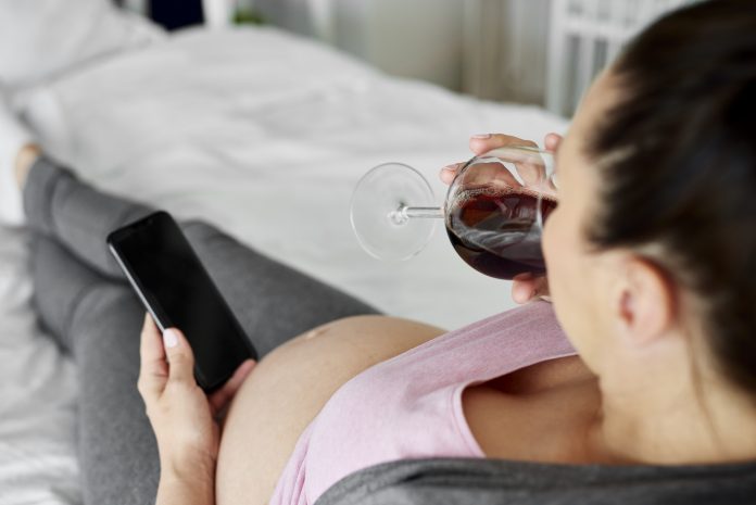 Heavily pregnant woman drinking glass of red wine in bed