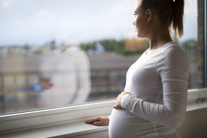 Heavily pregnant woman looking out the window