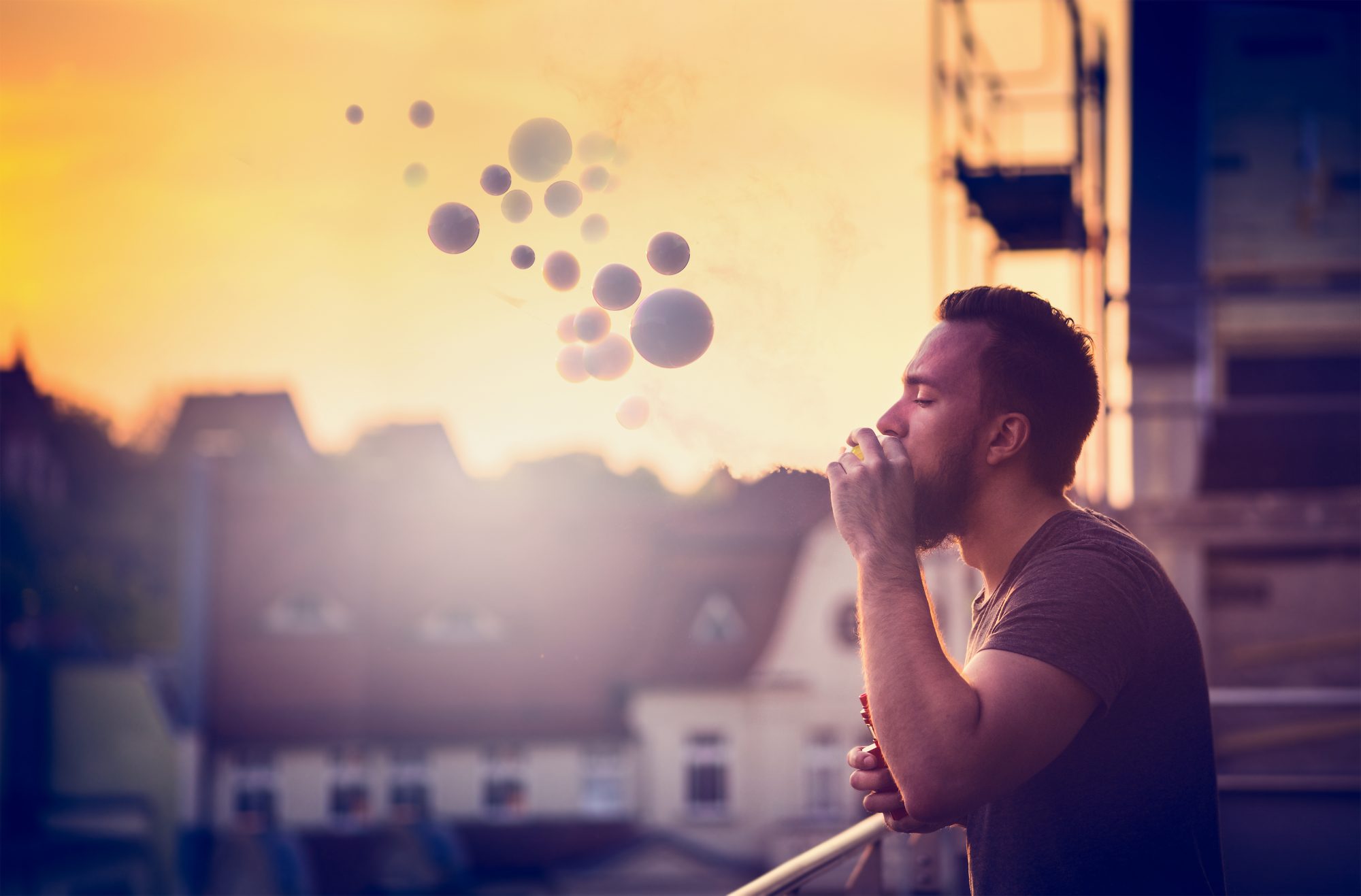 Young man with beard on blurry background sunset sky, making soap bubbles smoke inside with the aid of vape