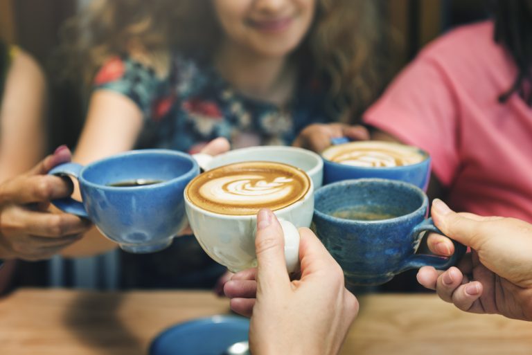 Women holding coffee cups together around table