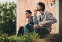 Two young men smoking cannabis, sat outside amongst greenery