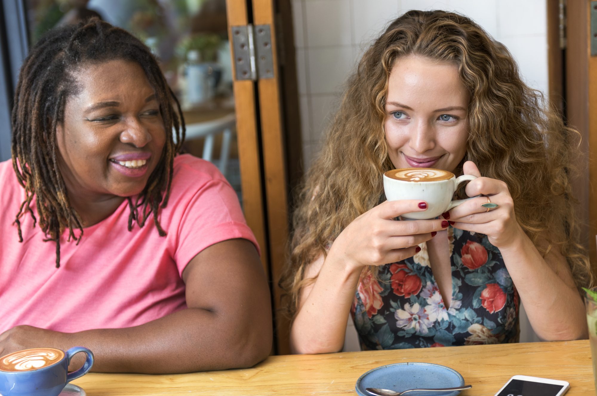 Two women sat round table smiling and drinking coffee