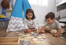 Two Children Playing Number Puzzle Game Together In Playroom, sitting in front of tent/tipi