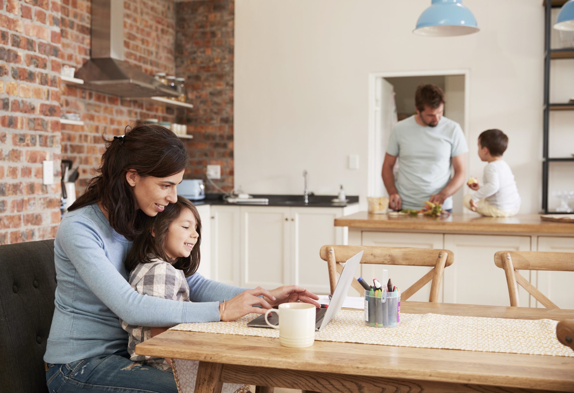 Family sitting in kitchen, mother and daughter sitting at laptop doing maths homework