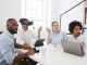 Man in VR goggles at a desk with colleagues in an office