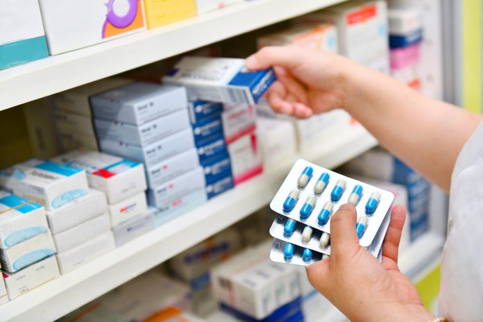 Pharmacist holding medicine box and capsule pack in pharmacy drugstore