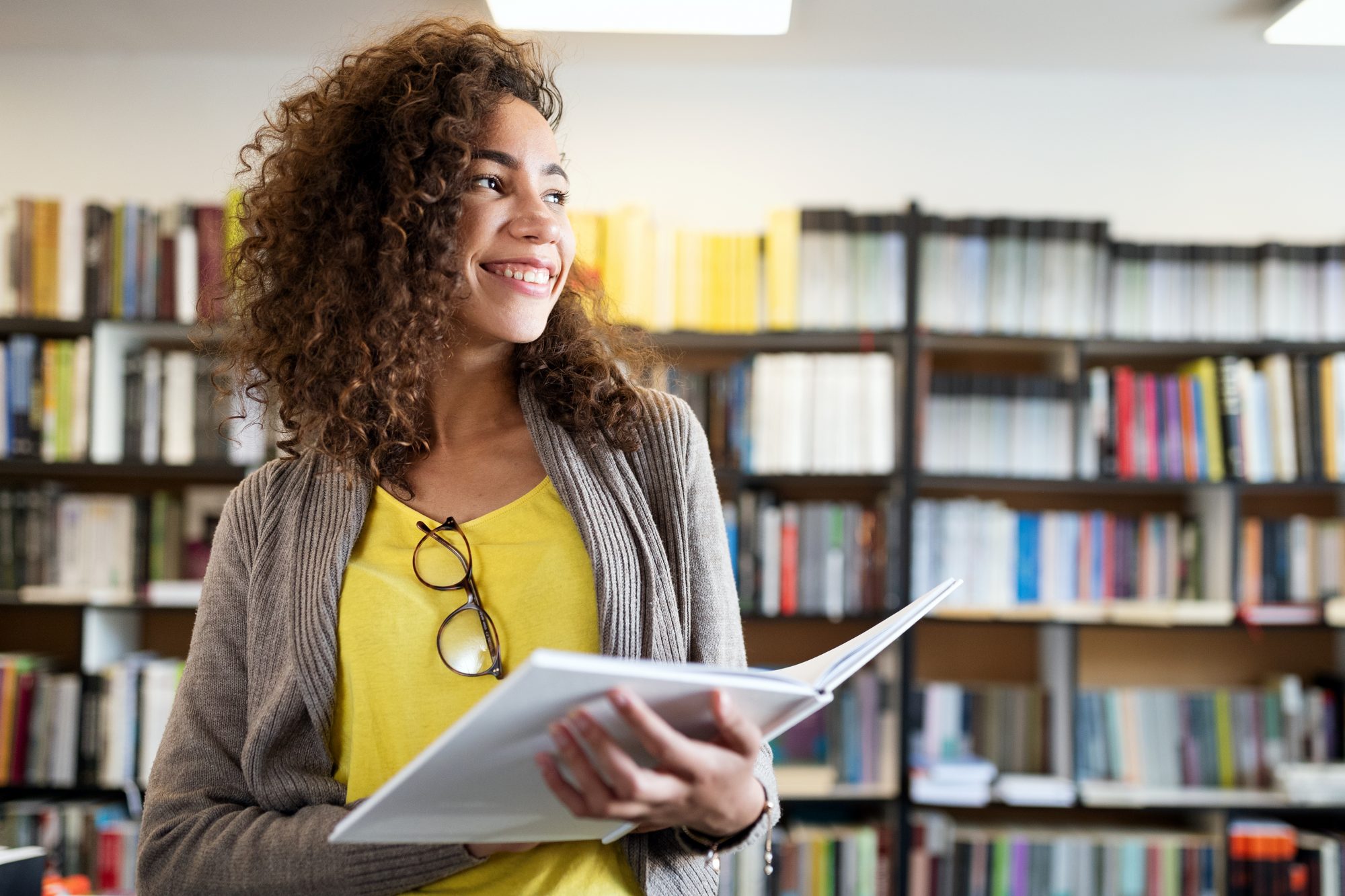 Young woman smiling and holding book in university library