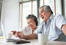 old Chinese couple using computer sat at dining table with mugs