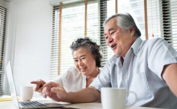 old Chinese couple using computer sat at dining table with mugs