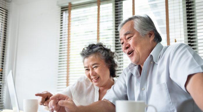 old Chinese couple using computer sat at dining table with mugs
