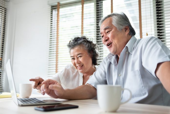 old Chinese couple using computer sat at dining table with mugs