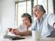 old Chinese couple using computer sat at dining table with mugs