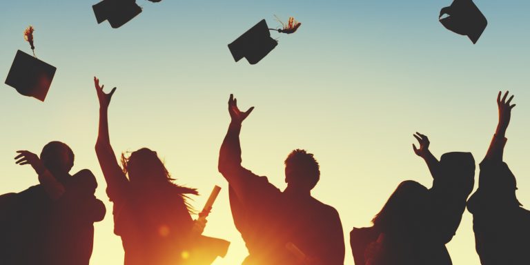 Silhouette of graduates throwing their caps up in the air against a beautiful sunset sky