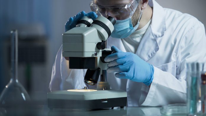 Male scientist looking into microscope for treatment vaccine