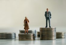 A miniature man and miniature woman standing on top of a pile of coins. The concept of the gender pay gap